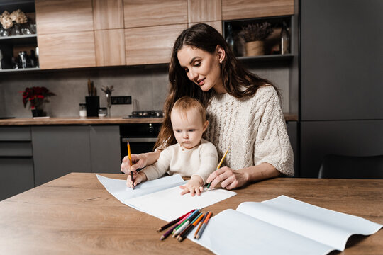 Mom and toddler daughter painting pictures with colored pencils and spend time with mother together. Developing drawing lesson for child toddler at home. Maternity leave.