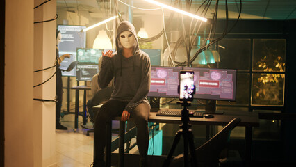 Dangerous masked adult broadcasting hacktivism video to receive ransom, stealing passwords and broadcasting live threat on dark web. Woman with anonymous mask doing illegal activity at night.