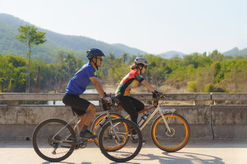 Asian cyclist couple riding together for exercise around the lake in the morning with beautiful mountain view in the background.