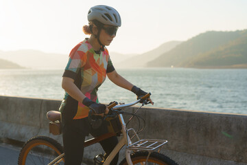 Asian cyclist woman prepares for exercise bike around the lake in the clear morning.