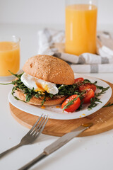 Breakfast sandwich with egg and arugula and cherry tomatoes on the table with orange juice