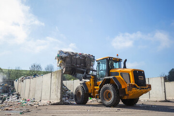 Front loader with scrap handling grapple bucket moving forward and backward to push, scoop and dump material at recycling and waste center