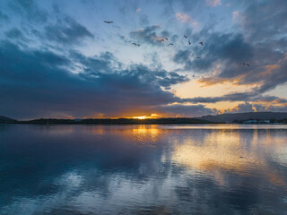 Sunrise waterscape with rain clouds, birds and reflections