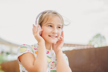 Close-up little cute girl laughing happily enjoying listening to music in headphones and phone outdoors in summer