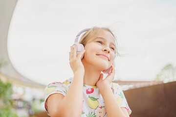 Close-up little cute girl laughing happily enjoying listening to music in headphones and phone outdoors in summer