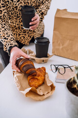 Woman at the workplace has a lunch of brown and chocolate croissants with coffee, food delivery concept