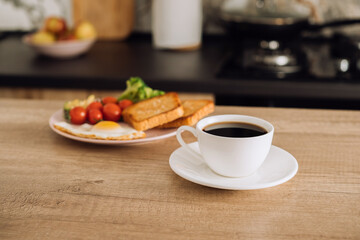 Cup of black coffee and breakfast in the background in the kitchen at home