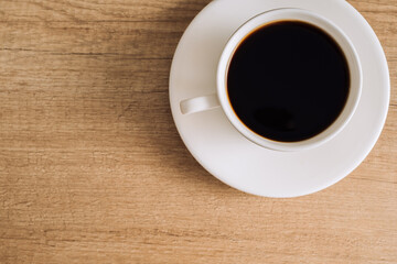Black coffee in a white cup with a saucer on a wooden table