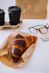 Delicious chocolate and brown croissants and coffee cups at workplace with glasses and notebook, food delivery concept