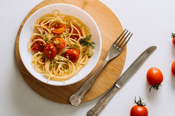 Flat lay portion of spaghetti pasta with cherry tomatoes sprinkled with spices in a plate on a wooden board