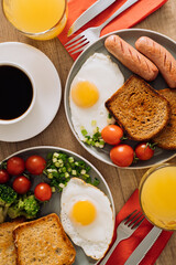 Flat lay English breakfast with cup of black coffee and orange juice, grilled sausage and whole wheat toast with fried egg and cherry tomatoes