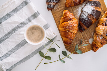 Cup of cappuccino with kitchen towel and eucalyptus branch, brown croissants on the cutting board