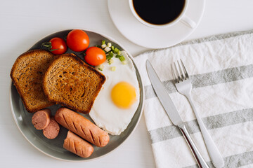 Breakfast plate with cup of black coffee, grilled sausage and whole wheat toast with fried egg and cherry tomatoes on a plate