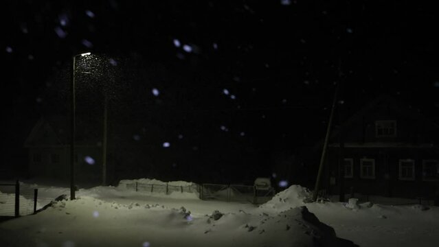Night snowfall in countryside with street lighting.