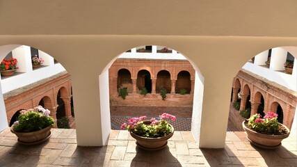  View through the white arches of the upper level of the Mudejar cloister at La Rábida Franciscan Friary decorated by colorful geraniums in winter sun, Palos de la Frontera, Spain