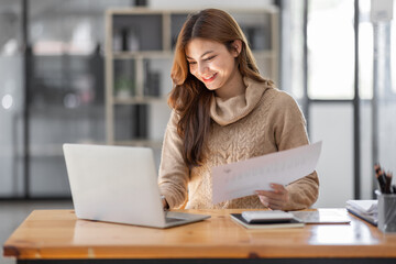 Asian Businesswoman Using laptop computer and working at office with calculator document on desk, doing planning analyzing the financial report, business plan investment, finance analysis concept.