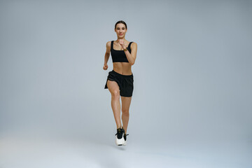 Athletic active woman wearing sportswear running on studio background. Dynamic movement