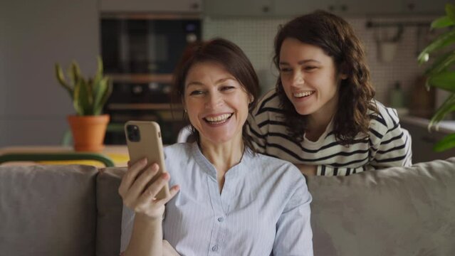 Happy mom and adult daughter make video calls while at home and sitting on the couch. Cozy atmosphere to call loved ones, relatives and friends and wishing happy holidays. communication at a distance