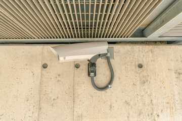 Wall-mounted security camera under a ceiling with screen metal at Austin, Texas. CCTV mounted on a concrete wall in a close-up view.