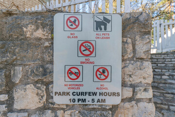 Park rules sign on a rough stone wall in a park at Austin, Texas. Signage with No glass, pets,...