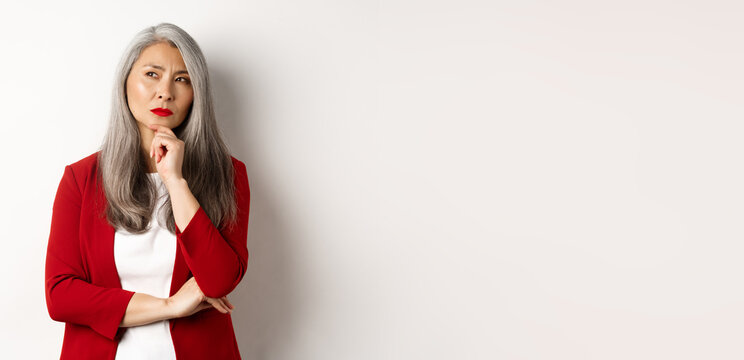 Business Concept. Thoughtful Senior Asian Businesswoman Looking Aside, Thinking While Standing Over White Background