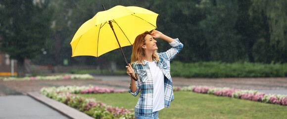 Happy young woman with umbrella under autumn rain in park. Banner design