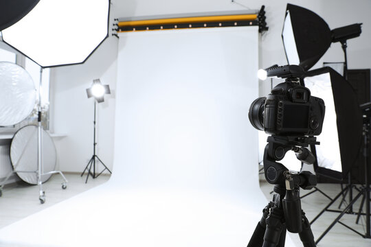 Tripod with camera and professional lighting equipment in modern photo studio. Space for text