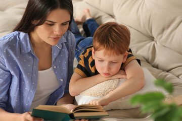 Mother reading book with her son in living room at home