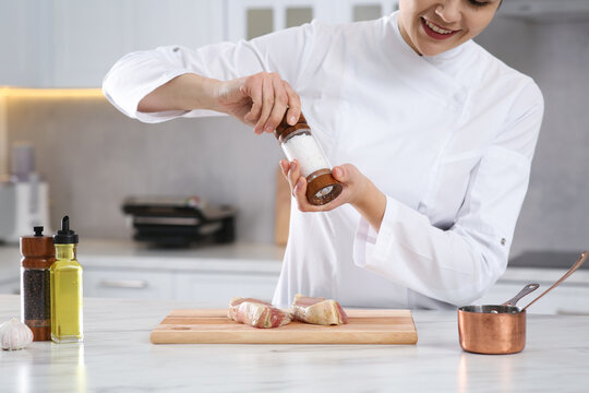 Professional chef adding pepper to delicious meat at white marble table, closeup