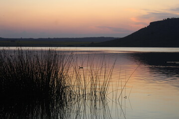 Atardecer en una hermosa laguna, junto a sierras y plantas