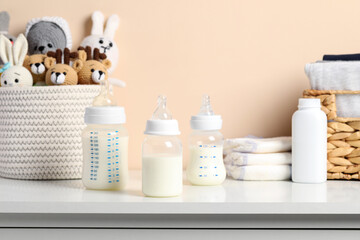 Fototapeta na wymiar Feeding bottles with milk and other baby accessories on white table near beige wall