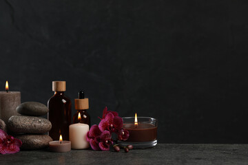 Beautiful composition with burning candles, spa stones and different care products on dark grey...