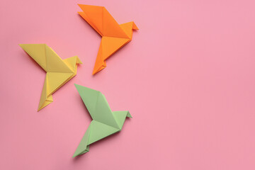 Beautiful colorful origami birds on pink background, flat lay. Space for text