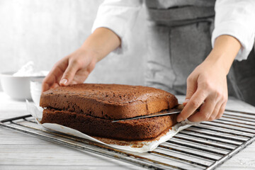 Woman cutting homemade chocolate cake into layers at white wooden table, closeup