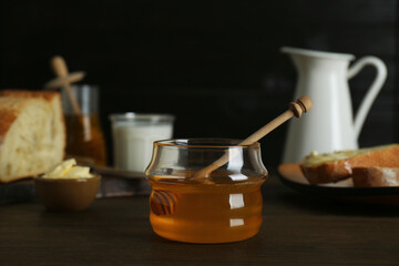 Jar with honey, milk, bread and butter on wooden table