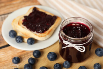 Jar of delicious blueberry jam and fresh berries on wooden table, closeup. Space for text