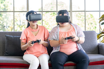 mother and daughter wearing virtual reality headset and playing game controller on sofa at home