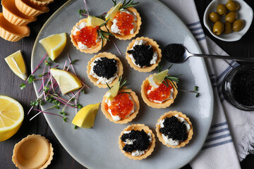 Delicious tartlets with red and black caviar served on wooden table, flat lay