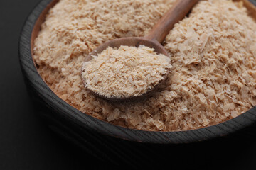 Bowl and spoon of brewer`s yeast flakes on black background, closeup
