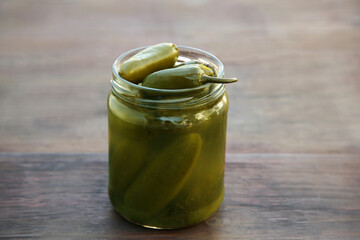 Glass jar of pickled green jalapeno peppers on wooden table, closeup