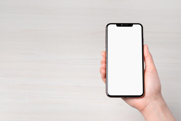 Woman holding smartphone with blank screen at white wooden table, top view. Mockup for design