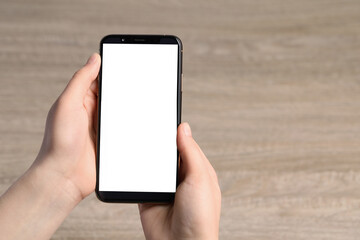 Woman holding smartphone with blank screen at wooden table, top view. Mockup for design