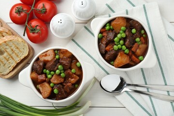 Delicious beef stew with carrots, peas and potatoes served on white wooden table, flat lay