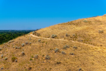 Hiking trail in the middle of a mountain slope in Boise, Idaho. Mountain trail on a slope with views of trees on the left against the clear blue skies.