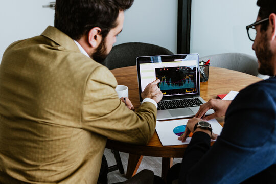 hispanic couple of business men and market investors discussing trading charts using computer and looking at screen analyzing invest strategy and financial risks at office in Mexico Latin America
