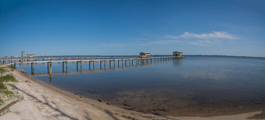 Fototapeta premium Private docks with boat lifts against the blue sky background at Navarre, Florida. Views of dock from a shore with sand and grasses at the front.