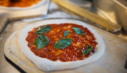 Prepared uncooked raw making pizza Margherita plant-based, with tomato sauce, mozzarella, and basil leaves on a board, close up of making process. 