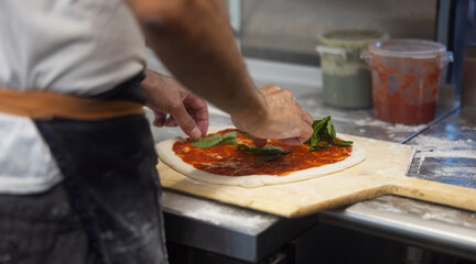 Prepared uncooked raw making pizza Margherita plant-based, with tomato sauce, mozzarella, and basil leaves on a board, hands in flour close up of making process. 
