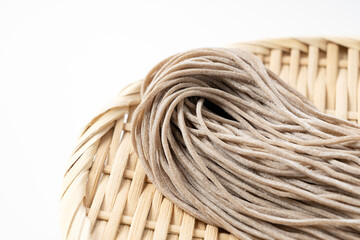 Raw soba noodles in a bamboo colander placed against a white background.