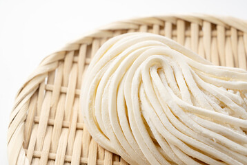 Fresh udon noodles in a bamboo colander placed on a white background.